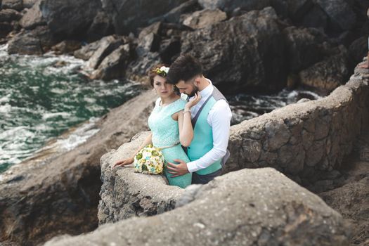 The bride and groom on nature in the mountains near the water. Suit and dress color Tiffany. Kiss and hug.