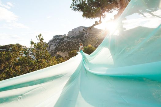 Bride in nature in the mountains near the water. Dress color Tiffany. The bride is playing with his dress.