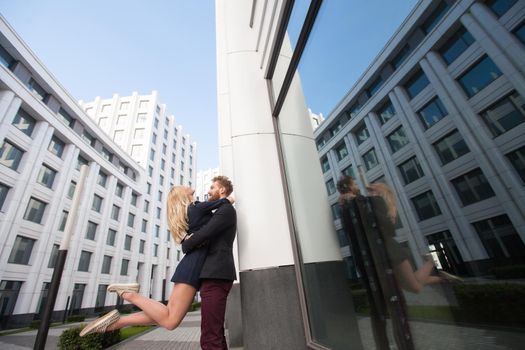 Guy hugging a girl in the city on the background of buildings. The reflection in the glass
