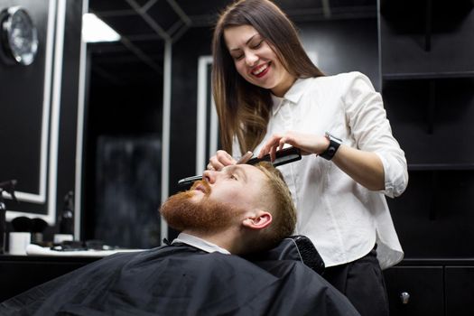 stylist girl shaves beard man in Barbershop