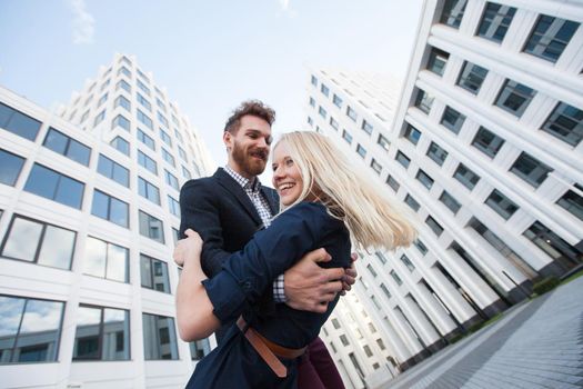 Man and woman hugging and laughing in front of a white building. Bottom view