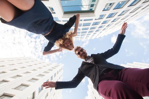 Cheerful young couple fooling around, jumping on the background of the building. Bottom view