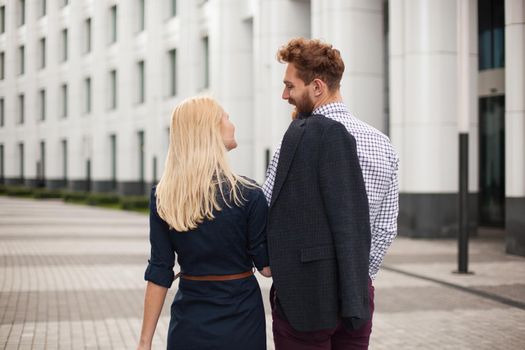 Rear view of young couple man and woman looking at each other. The white building in the background.