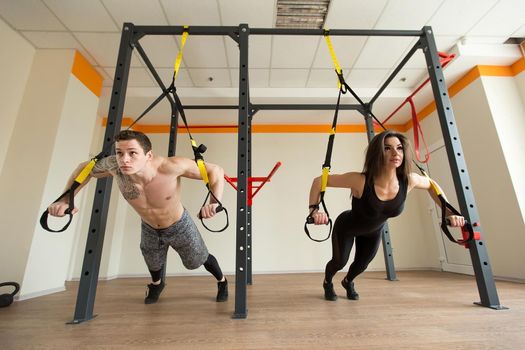 Young woman and man training exercise push ups with trx fitness straps in the gym Concept sport workout healthy lifestyle.