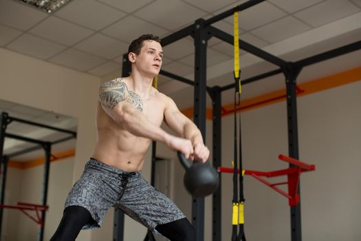 Beautiful man squats with kettlebell at the gym