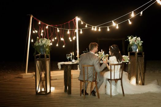 The night wedding ceremony. The bride and groom are sitting at the festive table. Banquet