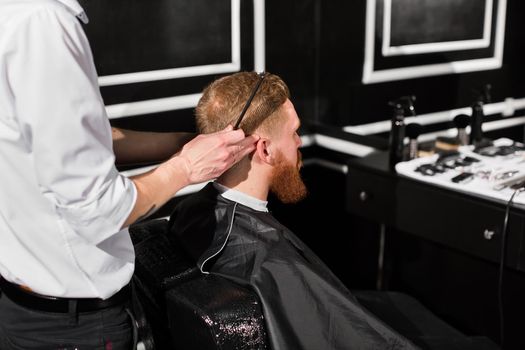 Master cuts hair and beard in the Barber shop. Hairdresser makes hairstyle using scissors and a metal comb.
