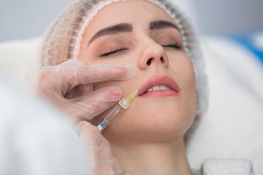 Hands of cosmetologist making injection in face, lips. Young woman gets beauty facial injections in salon. Face aging, rejuvenation and hydration procedures. Aesthetic cosmetology.