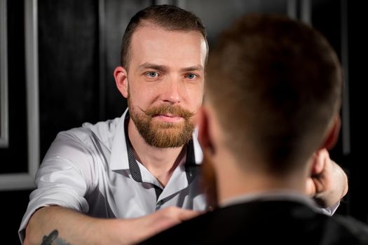 Master cuts hair and beard in the Barber shop. Hairdresser makes hairstyle using scissors and a metal comb.