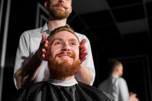 Master cuts hair and beard in the Barber shop. Hairdresser makes hairstyle using scissors and a metal comb. A satisfied customer.