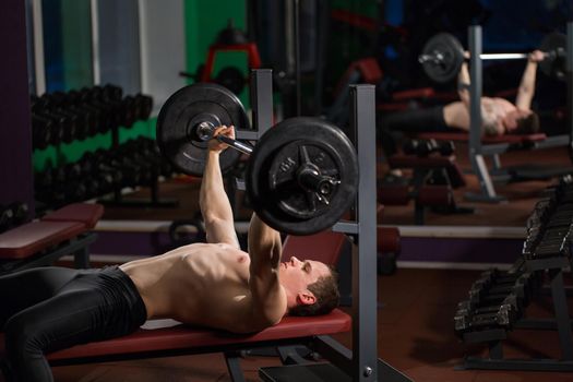 Brutal athletic man pumping up muscles on bench press