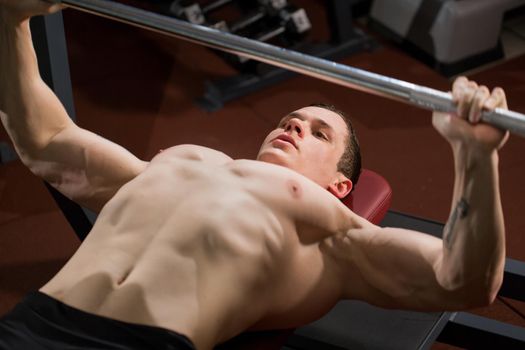 Brutal athletic man pumping up muscles on bench press