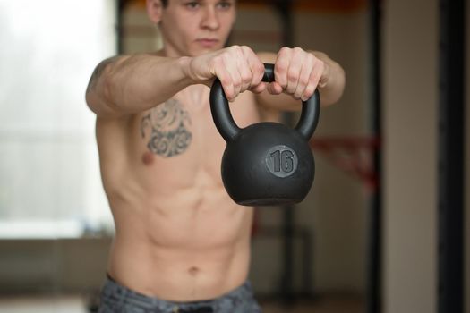 Beautiful man squats with kettlebell at the gym