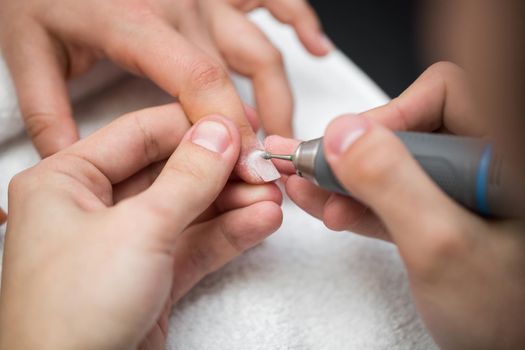 The master uses an electric machine to remove the nail polish during manicure in the salon. Hardware manicure. Concept of body care