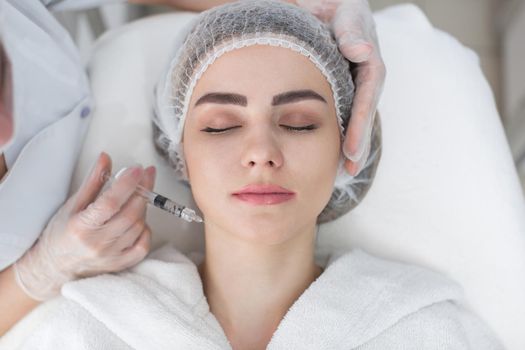 Hands of cosmetologist making injection in face, lips. Young woman gets beauty facial injections in salon. Face aging, rejuvenation and hydration procedures. Aesthetic cosmetology.