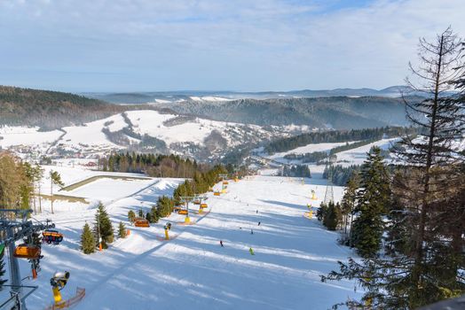 Skiers go down the slope at Slotwiny Arena ski station on a sunny day, Krynica Zdroj, Poland