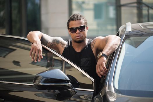 An African-American man poses near his car