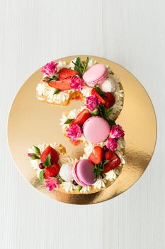 The cake with cheese cream and honey cakes is decorated with flowers, berries and sweets. A cake in the shape of the number 3.