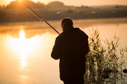 The angler fishing with spinning on the pond, the lake at sunset