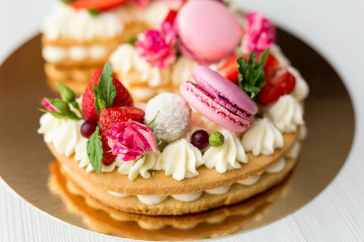 The cake with cheese cream and honey cakes is decorated with flowers, berries and sweets. A cake in the shape of the number 3.