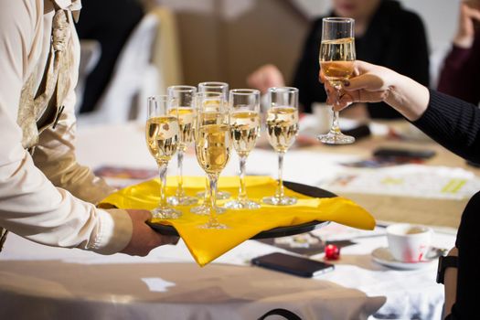 Waiter served champagne glasses on a tray in a fine dining restaurant and woman takes a glass