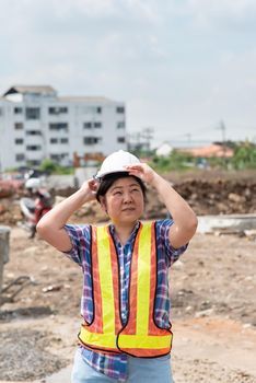 Asian woman civil construction engineer worker or architect with helmet and safety vest happy working at a building or construction site