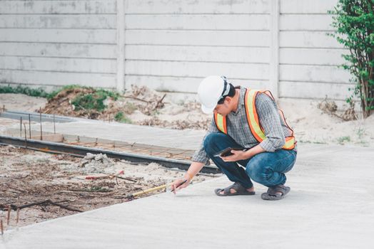 Asian man civil construction engineer worker or architect with helmet and safety vest working and holding a touchless tablet computer for see blueprints or plan at a building or construction site