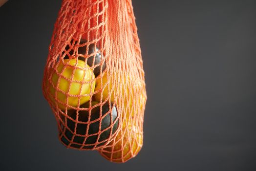 fresh orange fruit and avocado in a shopping bag against black background .
