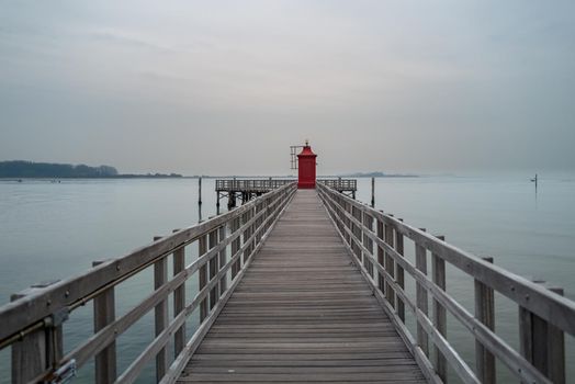 A small red lighthouse at the end of a cold foggy winter day.