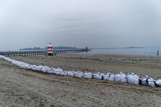 Wintry sandy beach without people with a small lighthouse and sandbags as protection against the water.