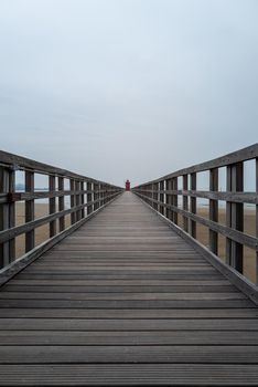 Small red old lighthouse at the end of a long jetty from a low perspective.