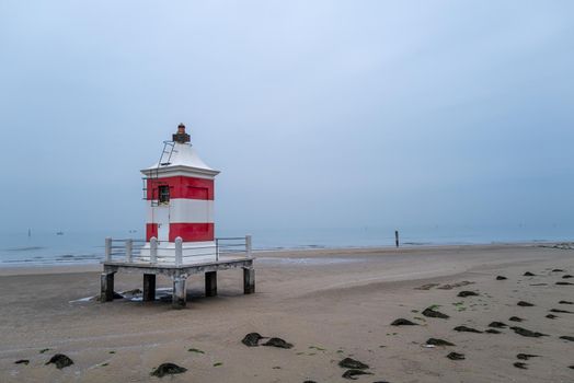 Small red white wooden lighthouse on wintry sandy beach without people.