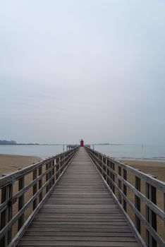 Small red old lighthouse at the end of a long jetty from a high perspective.