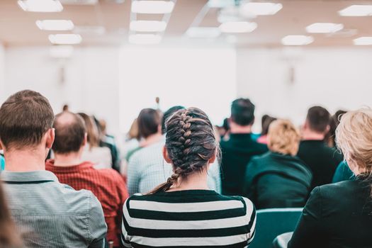 Business and entrepreneurship symposium. Speaker giving a talk at business meeting. Audience in conference hall. Rear view of unrecognized participant in audience.