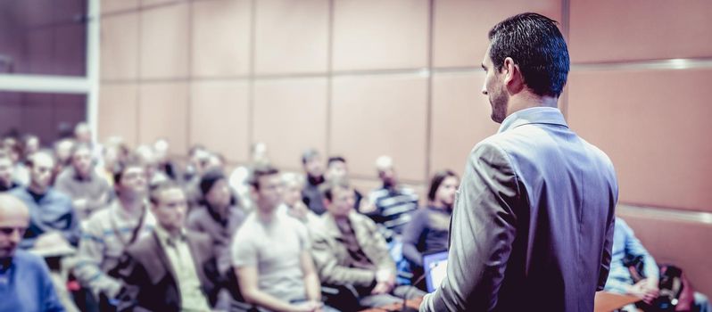 Speaker giving a talk on corporate business conference. Unrecognizable people in audience at conference hall. Business and Entrepreneurship event.