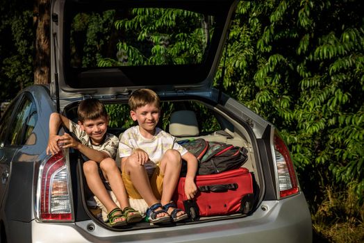 Two cute boys sitting in a car trunk before going on vacations with their parents. Two kids looking forward for a road trip or travel. Summer break at school. Family travel by car.