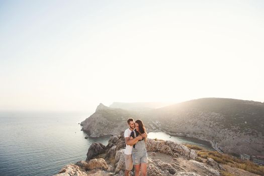 Guy hugs a girl on the edge of a rock close up against the background of a mountain
