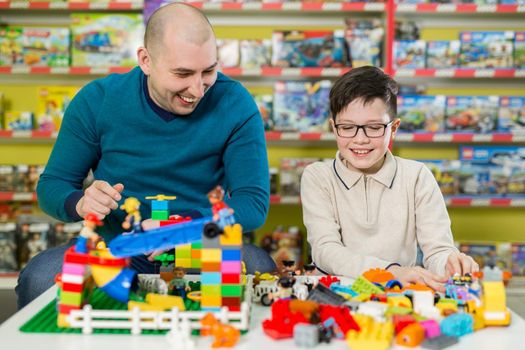 Father and son with happy faces create colorful constructions of toy bricks. Dad and kid build of plastic blocks. Family and childhood concept.
