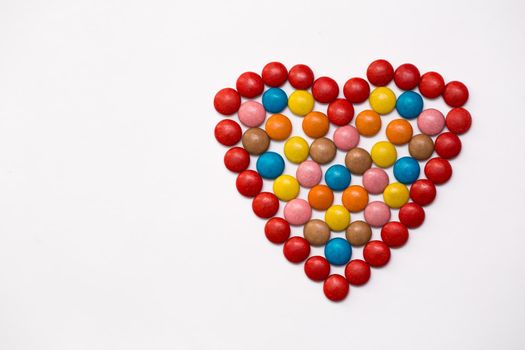 Colorful button chocolate candies in the love shape on white background