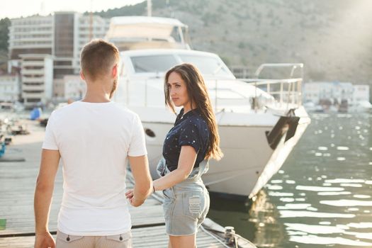 Lovers walk on the pier against the backdrop of yachts and boats.