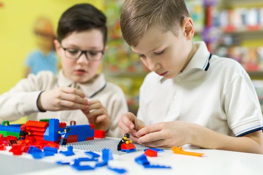 Children play in the designer at the table. Two boys play together with colored plastic blocks in the gaming center, school.