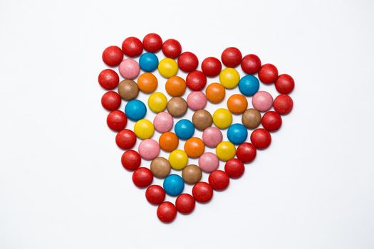 Colorful button chocolate candies in the love shape on white background