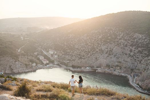 Lovers, guy and girl, on the edge of the cliff against the backdrop of mountains and ocean.