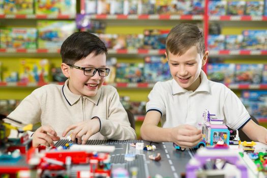 Children play in the designer at the table. Two boys play together with colored plastic blocks in the gaming center, school.