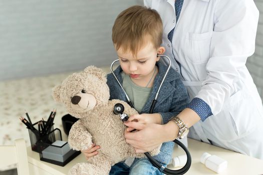 Doctor and boy patient examining teddy bear in Hospital