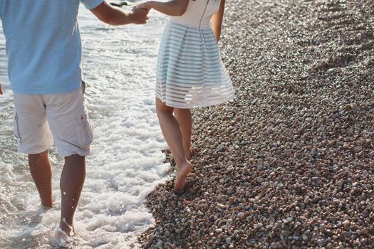 Couple holding hands walking on the pebbles near the sea