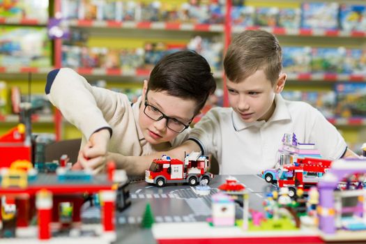 Children play in the designer at the table. Two boys play together with colored plastic blocks in the gaming center, school.