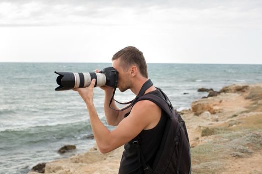 A photographer with a backpack on the cliff taking pictures of the sea