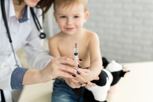 Doctor pediatrician plays before the injection with the boy.