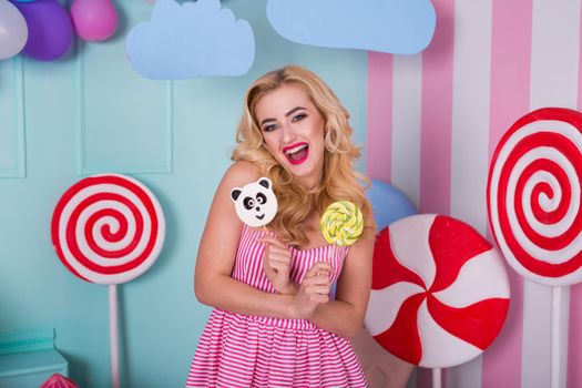 Portrait of amazing sweet-tooth woman in pink dress holding candies and posing on background decorated with huge ice cream. Lollipop panda